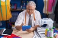 Middle age grey-haired man tailor using touchpad at tailor shop