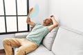 Middle age grey-haired man using handfan sitting on sofa at home Royalty Free Stock Photo