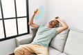 Middle age grey-haired man using handfan sitting on sofa at home Royalty Free Stock Photo