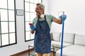 Middle age grey-haired man using smartphone cleaning at home