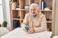 Middle age grey-haired man using smartphone sitting on table at home Royalty Free Stock Photo
