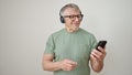 Middle age grey-haired man using smartphone wearing headphones over isolated white background Royalty Free Stock Photo
