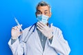 Middle age grey-haired man wearing doctor uniform and medical mask holding syringe covering mouth with hand, shocked and afraid Royalty Free Stock Photo