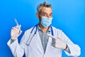 Middle age grey-haired man wearing doctor uniform and medical mask holding syringe smiling happy pointing with hand and finger Royalty Free Stock Photo