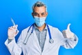 Middle age grey-haired man wearing doctor uniform and medical mask holding syringe smiling happy and positive, thumb up doing Royalty Free Stock Photo