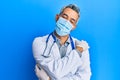 Middle age grey-haired man wearing doctor uniform and medical mask hugging oneself happy and positive, smiling confident Royalty Free Stock Photo