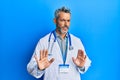 Middle age grey-haired man wearing doctor uniform and stethoscope disgusted expression, displeased and fearful doing disgust face