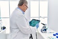 Middle age grey-haired man wearing scientist uniform looking embryology image touchpad at laboratory