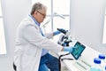 Middle age grey-haired man wearing scientist uniform looking embryology image touchpad at laboratory Royalty Free Stock Photo