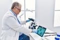 Middle age grey-haired man wearing scientist uniform looking embryology image touchpad at laboratory