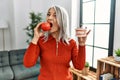 Middle age grey-haired woman bitting red apple and holding denture at home