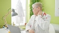 Middle age grey-haired woman doctor tired stretching neck working at clinic Royalty Free Stock Photo