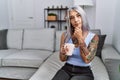 Middle age grey-haired woman drinking coffee sitting on the sofa at home looking confident at the camera smiling with crossed arms Royalty Free Stock Photo