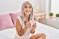 Middle age grey-haired woman drinking cup of coffee sitting on bed at bedroom Royalty Free Stock Photo