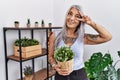 Middle age grey-haired woman holding green plant pot at home doing peace symbol with fingers over face, smiling cheerful showing Royalty Free Stock Photo