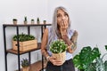 Middle age grey-haired woman holding green plant pot at home laughing and embarrassed giggle covering mouth with hands, gossip and Royalty Free Stock Photo