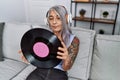 Middle age grey-haired woman listening to music holding vinyl disc at home relaxed with serious expression on face