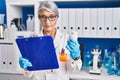 Middle age grey-haired woman scientist reading document holding pills bottle at laboratory Royalty Free Stock Photo