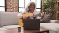 Middle age grey-haired woman smiling confident having online guitar class at home