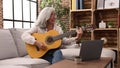 Middle age grey-haired woman smiling confident having online guitar class at home