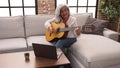 Middle age grey-haired woman smiling confident having online guitar class at home