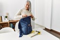 Middle age grey-haired woman smiling confident preparing trip backpack at home