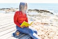 Middle age grey-haired woman smiling happy reading book at the beach Royalty Free Stock Photo