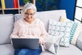 Middle age grey-haired woman using laptop sitting on sofa at home Royalty Free Stock Photo