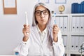 Middle age grey-haired woman working at dentist clinic holding electric teethbrush and toothbrush puffing cheeks with funny face Royalty Free Stock Photo