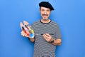 Middle age handsome artist man wearing french beret drawing using paintbrush and palette looking positive and happy standing and