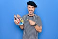 Middle age handsome artist man wearing french beret drawing using paintbrush and palette smiling happy pointing with hand and