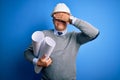 Middle age handsome grey-haired architect man wearing safety helmet holding blueprints covering eyes with hand, looking serious Royalty Free Stock Photo