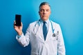 Middle age handsome grey-haired doctor man holding smartphone showing screen with a confident expression on smart face thinking Royalty Free Stock Photo