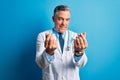 Middle age handsome grey-haired doctor man wearing coat and blue stethoscope doing money gesture with hands, asking for salary Royalty Free Stock Photo