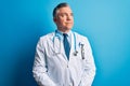 Middle age handsome grey-haired doctor man wearing coat and blue stethoscope smiling looking to the side and staring away thinking Royalty Free Stock Photo