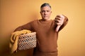 Middle age handsome grey-haired man doing housework holding wicker basket with clothes with angry face, negative sign showing