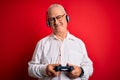 Middle age handsome hoary gamer man playing video game using joystick and headphones with a happy face standing and smiling with a