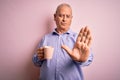 Middle age handsome hoary man drinking mug of coffee over isolated pink background with open hand doing stop sign with serious and