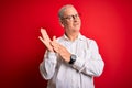 Middle age handsome hoary man wearing casual shirt and glasses over red background clapping and applauding happy and joyful,