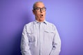 Middle age handsome hoary man wearing striped shirt and glasses over purple background afraid and shocked with surprise