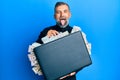 Middle age handsome man holding briefcase full of dollars sticking tongue out happy with funny expression Royalty Free Stock Photo