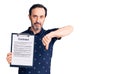 Middle age handsome man holding clipboard with contract document with angry face, negative sign showing dislike with thumbs down,