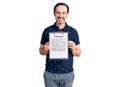 Middle age handsome man holding clipboard with contract document looking positive and happy standing and smiling with a confident