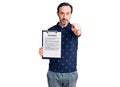 Middle age handsome man holding clipboard with contract document pointing with finger to the camera and to you, confident gesture