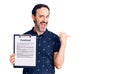 Middle age handsome man holding clipboard with contract document pointing thumb up to the side smiling happy with open mouth