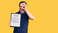 Middle age handsome man holding clipboard with contract document smiling happy doing ok sign with hand on eye looking through