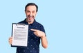 Middle age handsome man holding clipboard with contract document smiling happy pointing with hand and finger