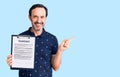 Middle age handsome man holding clipboard with contract document smiling happy pointing with hand and finger to the side