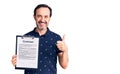Middle age handsome man holding clipboard with contract document smiling happy and positive, thumb up doing excellent and approval