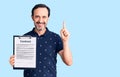 Middle age handsome man holding clipboard with contract document surprised with an idea or question pointing finger with happy